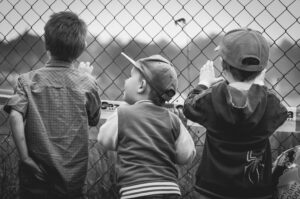 Tres niños pequeños con las manos en una valla, simbolizando la curiosidad y el aprendizaje, habilidades blandas fundamentales en el servicio al cliente.