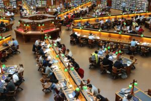 Estudiantes y profesionales dedicados al estudio y la investigación en una gran sala de lectura de biblioteca bien iluminada