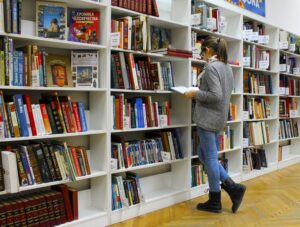 Una persona seleccionando un libro de una estantería en una biblioteca, simbolizando el aprendizaje continuo.