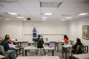 Un profesor observa a los estudiantes durante un examen en una sala de clase, destacando la importancia del aprendizaje continuo en la educación