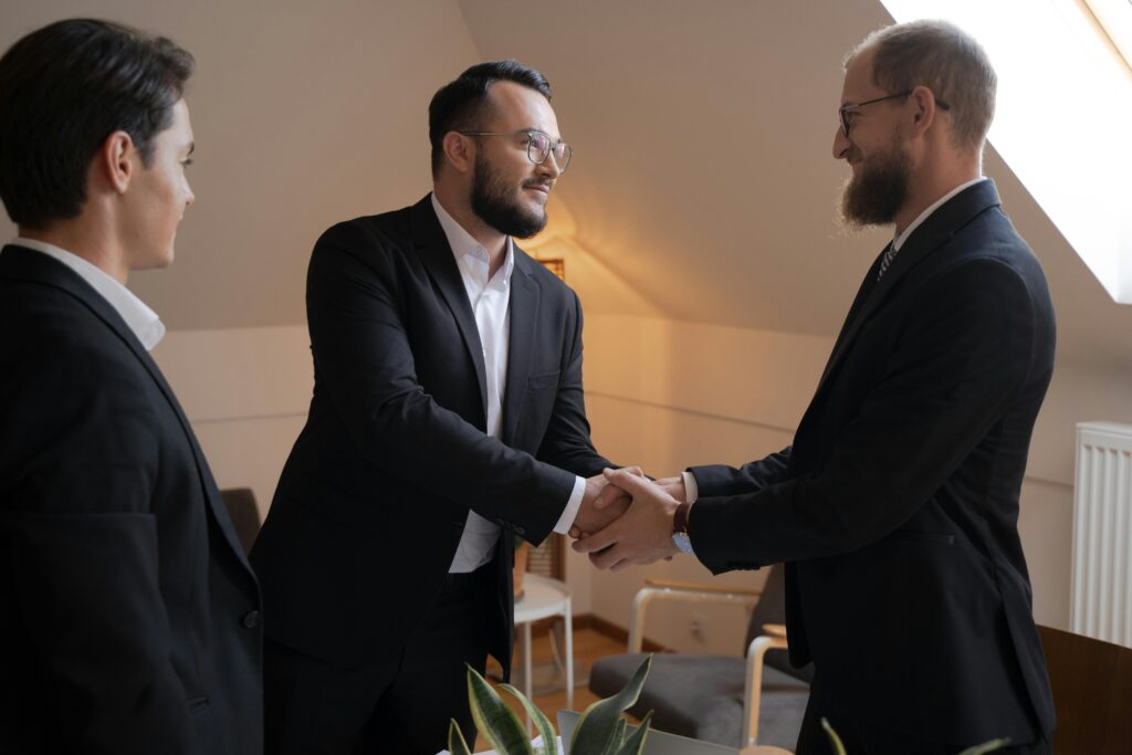 Dos profesionales estrechando manos en una oficina bien iluminada, con un colega observando.