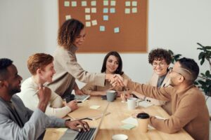 Un equipo diverso interactúa en una reunión, donde un apretón de manos celebra el éxito, un momento óptimo para evaluar habilidades blandas colaborativas.