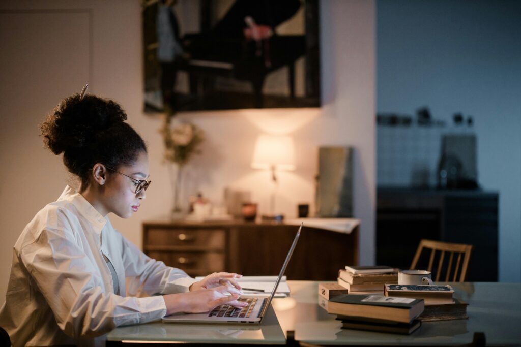 Una mujer concentrada trabaja en su laptop en un entorno hogareño, ilustrando la habilidad de autogestión y trabajo en solitario.