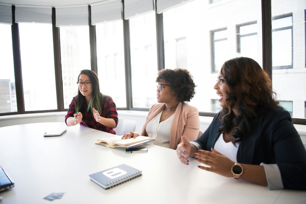 Tres mujeres en una reunión de trabajo, participando en una conversación activa, demostrando comunicación asertiva como una habilidad blanda clave.