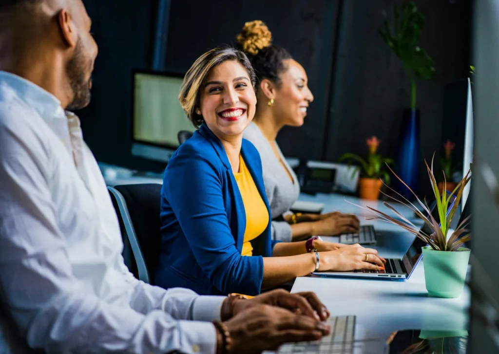 Un grupo diverso de profesionales sonriendo y trabajando juntos en un ambiente de oficina vibrante, ejemplificando la armonía del equipo mejorada por habilidades blandas.